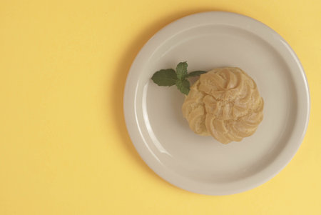 Kue Soes or choux Ã  la crÃ¨me isolated on a yellow background. Perfectly puffed and filled with a creamy filling, this classic French dessert is sure to delight. Selective Focus , Closeupの写真素材