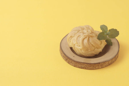 Kue Soes or choux Ã  la crÃ¨me isolated on a yellow background. Perfectly puffed and filled with a creamy filling, this classic French dessert is sure to delight. Selective Focus , Closeupの写真素材