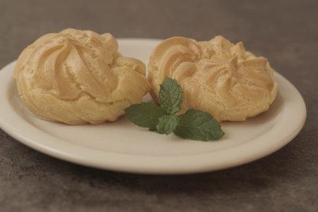 Kue Soes or choux Ã  la crÃ¨me on white plate. Perfectly puffed and filled with a creamy filling, this classic French dessert is sure to delight. Selective Focus , Closeupの写真素材