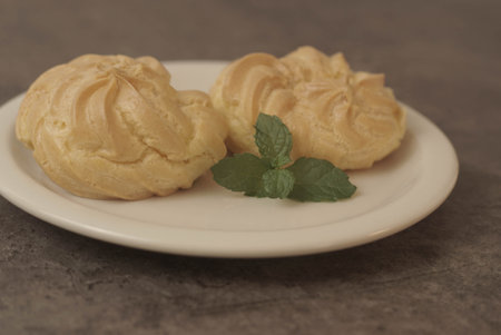 Kue Soes or choux Ã  la crÃ¨me on white plate. Perfectly puffed and filled with a creamy filling, this classic French dessert is sure to delight. Selective Focus , Closeupの写真素材