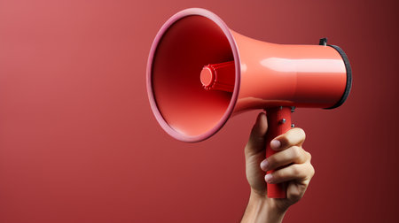 Close up of human hand holding megaphone over red background.の素材
