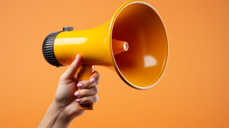 Female hand holding a megaphone on orange background with copy spaceの素材