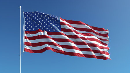 A vibrant American flag waves against a clear blue sky, symbolizing patriotism and freedom. The stars and stripes are crisp and bright.の素材