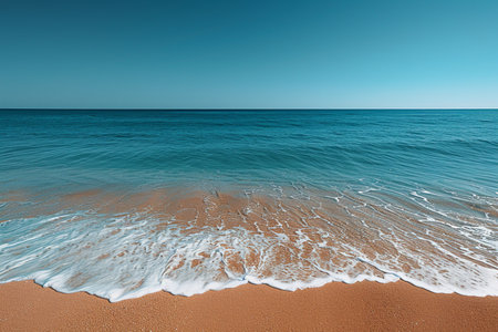 Serene beach scene with gentle ocean waves lapping on golden sand, under a vast, clear blue sky.の素材