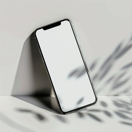 Minimalist mockup of a contemporary smartphone with a blank screen, elegantly positioned against a wall, casting subtle shadows.の素材