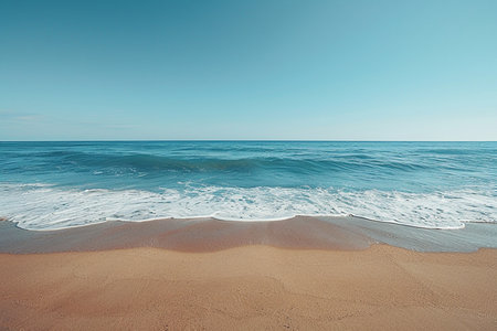 A tranquil scene of the ocean meeting a sandy beach, with calm waves and a vast, clear blue sky.の素材