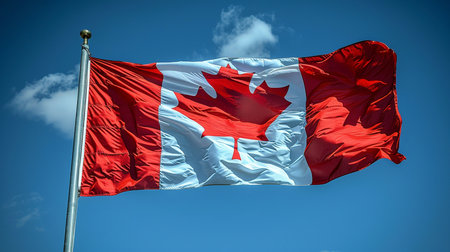 The iconic Canadian flag, featuring a red maple leaf on a white square between two red bars, waves in a clear blue sky with scattered white clouds.の素材