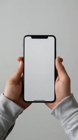 A person's hands hold a modern smartphone, showcasing its blank white screen. The phone is held horizontally.の素材