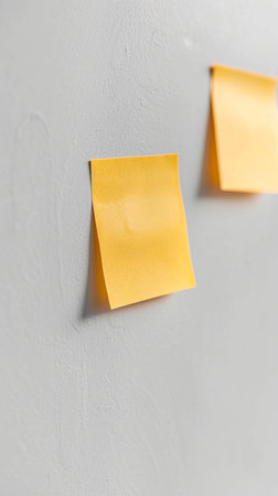 A textured gray wall with two bright yellow sticky notes. Perfect for notes, reminders, or background.の素材