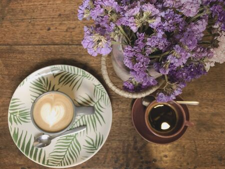 Cup of cappuccino with latte art and xpresso on a wooden plate and wooded table decorated with dried...