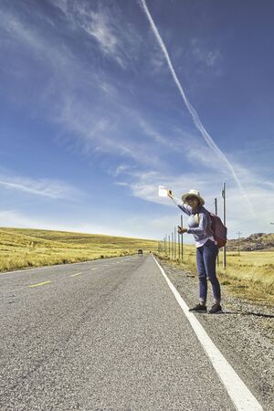 Beautiful woman hitchhiking on road in forest, hitchhiking with thumbs up in a countryside road, Traveling and hitchhiking concept.の写真素材