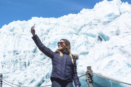 Beautiful girl in winter clothes takes a selfie at the Pastoruri Glacier, in the Huascarán National Park, Huaraz / Peru. Tropical glacier at 5200 meters above sea level.の写真素材