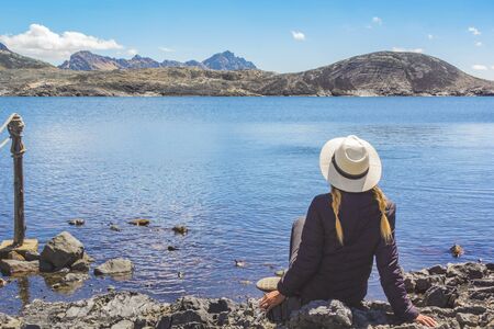 Beautiful woman sitting on the shore of the lake in front of the Pastoruri glacier, in the Huascaran National Park, Huaraz / Peru.の写真素材