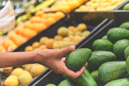 Young Woman Choosing Avocados in Grocery Store. Concept of healthy food, bio, vegetarian, diet. Selective focus.の写真素材