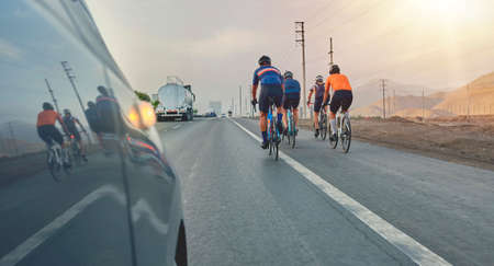Group of professional cyclists training on highway with safety escort car. A group of cyclists followed by team carsの写真素材