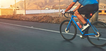 Cyclist man riding race bike on highway sunset.