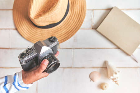 Top view of an analog camera and a notebook on a wooden table, photographer's hands hold old film camera on wooden background, travel outfit, concept travelの写真素材
