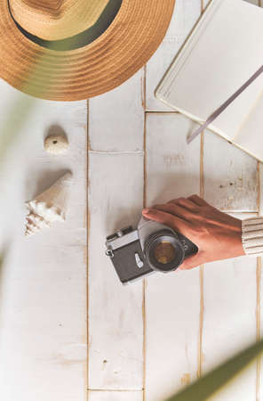Top view of an analog camera and a notebook on a wooden table, photographer's hands hold old film camera on wooden background, travel outfit, concept travelの写真素材