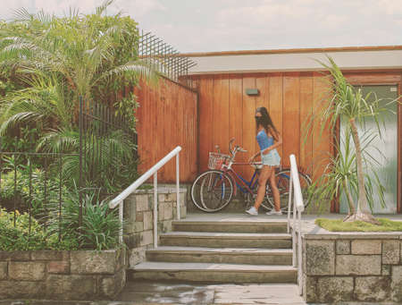 Young woman with protective mask leaving home to ride a bike on sunny summer day, AncÃ³n - Peru boulevard with palm trees flanking the beach, New normal conceptの写真素材