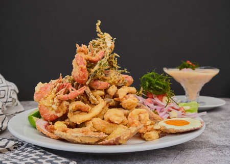 Peruvian food: chicharron de pez or fish cracklings with fried cassava and onion salad with chili, served on a white plate. Selective focusの写真素材