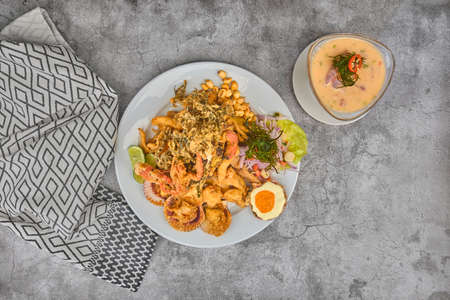 Peruvian food: chicharron de pez or fish cracklings with fried cassava and onion salad with chili, served on a white plate. Selective focusの写真素材