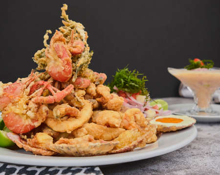 Peruvian food: chicharron de pez or fish cracklings with fried cassava and onion salad with chili, served on a white plate. Selective focusの写真素材