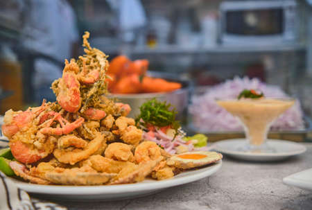 Peruvian food: chicharron de pez or fish cracklings with fried cassava and onion salad with chili, served on a white plate. Selective focusの写真素材