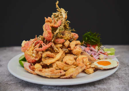 Peruvian food: chicharron de pez or fish cracklings with fried cassava and onion salad with chili, served on a white plate. Selective focusの写真素材
