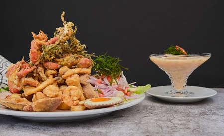 Peruvian food: chicharron de pez or fish cracklings with fried cassava and onion salad with chili, served on a white plate. Selective focusの写真素材