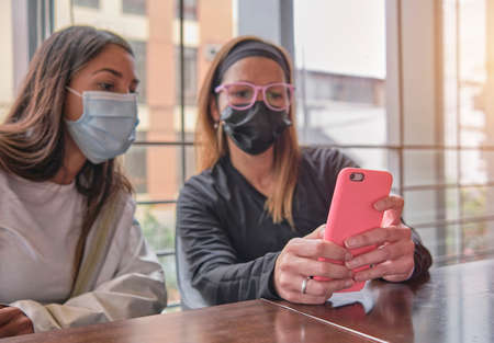 Two casual relaxed girls sitting together checking a mobile phoneの写真素材