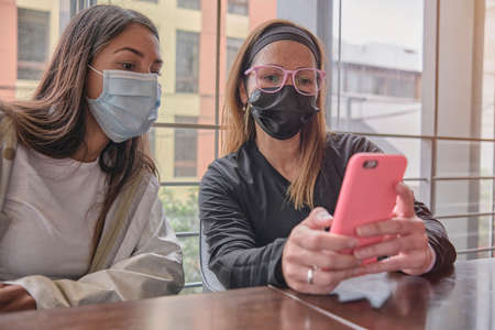 Two casual relaxed girls sitting together checking a mobile phoneの写真素材