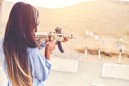 Woman empowered shooter aiming assault rifle at target. Selective Focus