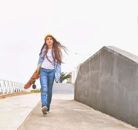 Girl having fun riding skateboards at skate park, Portrait of smiling young female skateboarder holding her skateboard. Recreational Activity Concept.の写真素材