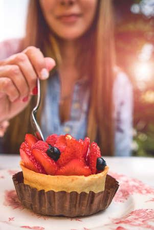 Young woman tasting strawberry-topped cake, Selective focus.の写真素材