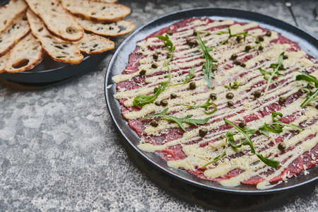 Beef Carpaccio cold appetizer with parmesan, capers and arugula on black plate, selective focusの写真素材