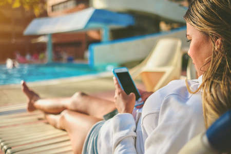 Young Beautiful using mobile phone sitting on chair in swimming pool.