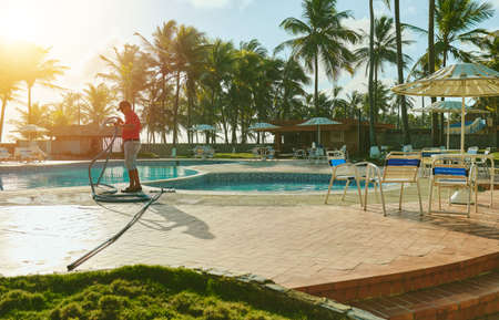 Worker cleaning outdoor pool with underwater vacuum early in the morning. Selective focus