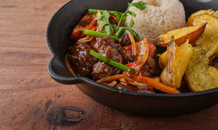 Peruvian d food - Lomo saltado - beef tenderloin with purple onion, yellow pepper, tomatoes served in a black pan with french fries and rice. Top viewの写真素材