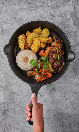 Peruvian d food - Lomo saltado - beef tenderloin with purple onion, yellow pepper, tomatoes served in a black pan with french fries and rice. Top viewの写真素材