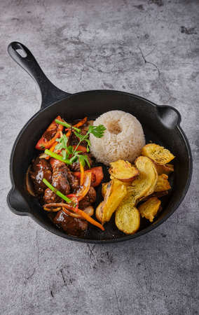 Peruvian d food - Lomo saltado - beef tenderloin with purple onion, yellow pepper, tomatoes served in a black pan with french fries and rice. Top viewの写真素材