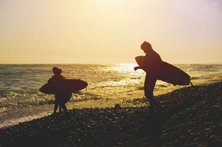 Silhouette Father And Son With Surfboard At Beach Against Sky During Sunset. Backlight during sunset...