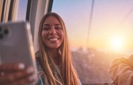 Young tourist sitting on the cableway in Caracas enjoying a photo taken on her smartphone. Bright sky, clouds and mountains. Selective focusの写真素材