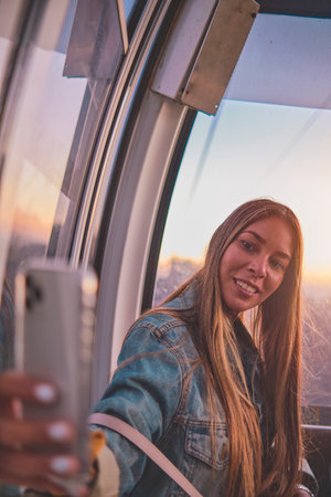 Young tourist sitting on the cableway in Caracas enjoying a photo taken on her smartphone. Bright sky, clouds and mountains. Selective focusの写真素材