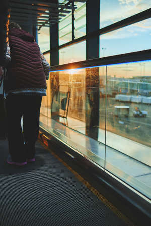 View on the aiport window with woman walking with suitcase at the departure hall during the sunset. Wide angle view with copy space.の写真素材
