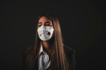 Executive young woman wearing medical mask with drawn smile on black backgroundの写真素材