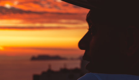 Back view backlight portrait of a single men watching a sunset on the sea with a warm light in the backgroundの写真素材