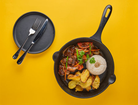 Peruvian d food - Lomo saltado - beef tenderloin with purple onion, yellow pepper, tomatoes served in a black pan with french fries and rice. Top viewの写真素材