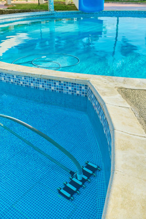 Worker cleaning outdoor pool with underwater vacuum early in the morning. Selective focus