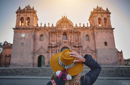 Young woman tourist in sunhat standing back in front of the main cathedral in Cusco, Peru.