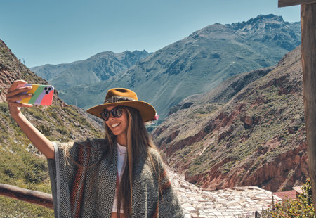 Traveler girl in hat and poncho doing selfie in Maras Salt Mines, Peru. Travel and wanderlust...